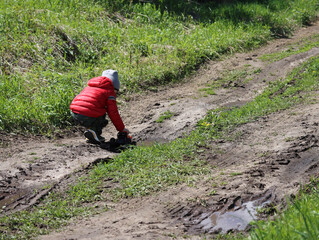 A boy in a red jacket plays with an orange toy monster truck