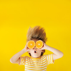 Surprized child holding slices of orange fruit like sunglasses - obrazy, fototapety, plakaty