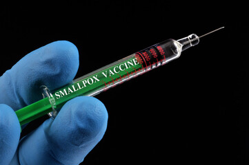 Concept de seringue de vaccin contre la variole dans une main gantée en gros plan sur fond noir