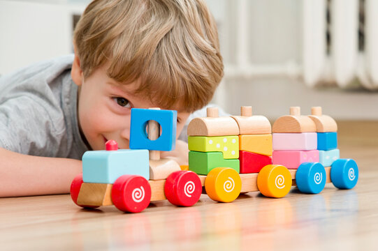 Boy sitting on the floor and playing with wooden colorful block train. Pre-school employment. Montessori concept. Brain and coordination exercise. Careless childhood.
