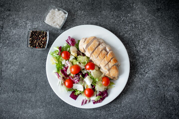 plate with chicken fillet and salad with vegetables on a stone background