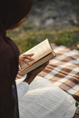 Portrait of a muslim woman sits on the plaid picnic blanket near the river