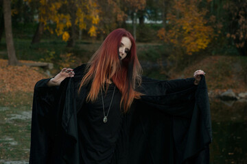 beautiful fashionable young girl witch model stands outdoors in the forest in autumn by the river,...