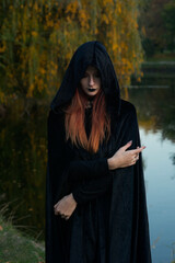 beautiful fashionable young girl witch model stands outdoors in the forest in autumn by the river,...