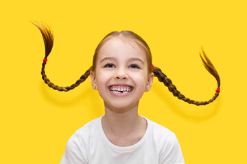 Cheerful child girl with growing teeth throws pigtails and laughs on a yellow background. Funny...