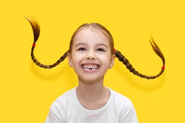 Fotobehang Cheerful child girl with growing teeth throws pigtails and laughs on a yellow background. Funny girl has fun and shows positive emotions by playing with her hair. Happy childhood concept © halcon1