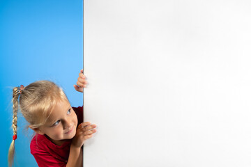 A cute mischievous cheerful girl peeks out from around the corner. White empty space for advertising. Poster mockup for website, sale page template.