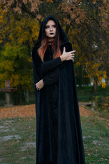 beautiful fashionable young girl witch model stands outdoors in the forest in autumn by the river,...