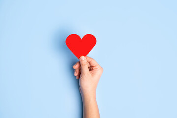Hand holding red paper heart on the blue background. With copy space. The concept of Valentine's Day.