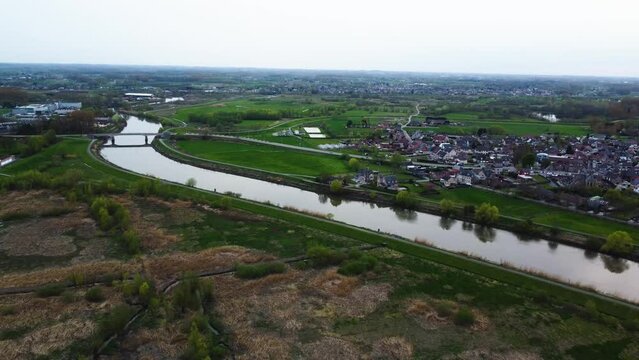 A drone pushes out in an aerial view of the river Shelde over green covered riverbank and a bridge.