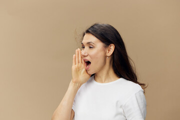 portrait of a woman in a white t-shirt standing sideways and screaming with her eyes closed standing on a beige background with empty space for an advertising mockup
