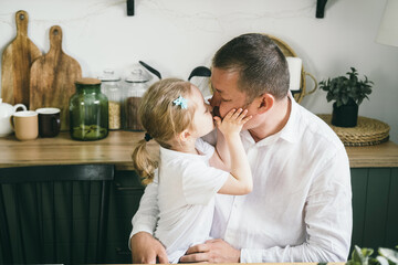 A little girl 4 years old gently hugs her dad. Daughter and dad at home in the kitchen. 