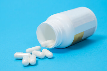 A jar of dietary supplements and white capsules on a blue background. Vitamins and trace elements for a complete diet