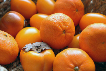 Persimmon, tangerines and yellow tomatoes in a jute basket. Orange fruits and vegetables. Ripe harvest.