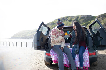 Happy couple drinking coffee at back of car on winter beach