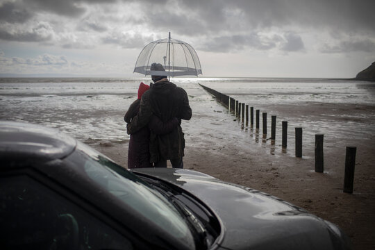 Couple under umbrella on wet stormy winter beach