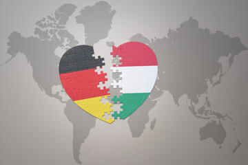 puzzle heart with the national flag of hungary and germany on a world map background. Concept.