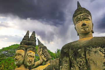 Mystical 4 stone buddha heads statues, dark storm clouds - Buddha Park (Wat Xieng Khuan),...