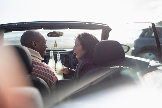 Happy couple drinking soda in sunny convertible