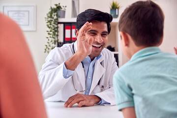 Doctor Or GP In White Coat Meeting Mother And Son For Appointment Giving Boy High Five