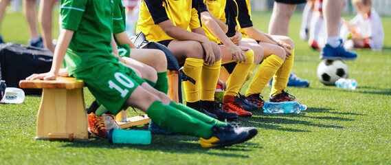 Football players are wearing soccer cleats and jersey kits in the youth team sitting on a wooden...