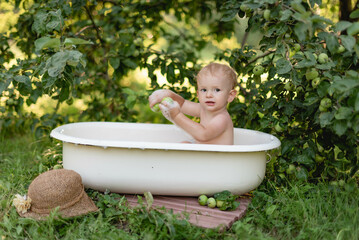 beautiful child bathes in white bath under tree in village