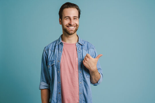 Young bristle man wearing shirt smiling and pointing finger aside