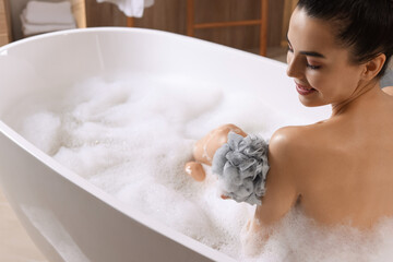 Woman taking bath with mesh pouf in tub