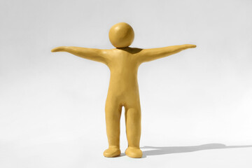 Human figure with arms wide open made of yellow plasticine on white background
