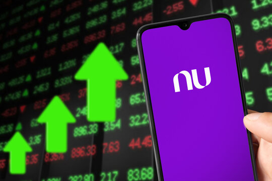 Smartphone with NuBank logo and background showing market value rising, 24 May, 2022, Sao Paulo, Brazil.