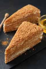 Slices of delicious layered honey cake served on black table, closeup