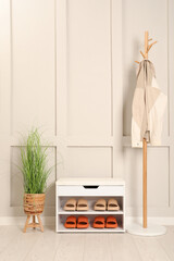 Stylish storage bench with different pairs of rubber slippers and beautiful houseplant near white wall in hall