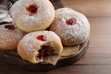 Delicious donuts with jelly and powdered sugar on wooden table, closeup