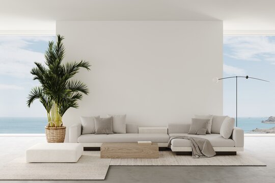 Aesthetic modern minimalist living room with a beige sofa and ocean views from the panoramic windows. Decor braided carpet on concrete floor and armchair, palm trees in a wicker pot