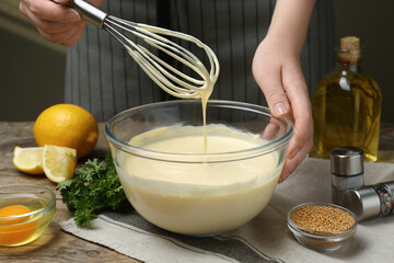 Woman making homemade mayonnaise in glass bowl at wooden table, closeup