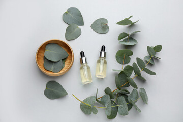 Flat lay composition with bottles of eucalyptus essential oil and plant branches on white background