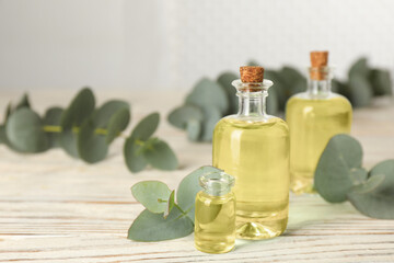 Eucalyptus essential oil and plant branches on white wooden table. Space for text