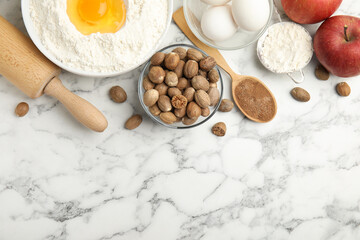 Nutmeg seeds and other ingredients on white marble table, flat lay. Space for text