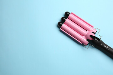 Modern triple curling hair iron on light blue background, top view. Space for text