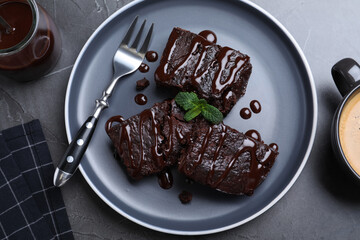 Delicious chocolate brownies with sweet syrup and mint served on grey table, flat lay