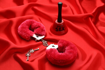Handcuffs, keys and bell with text Ring For Sex on red fabric