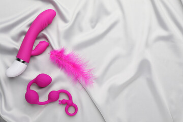 Pink sex toys and feather on white fabric, flat lay. Space for text