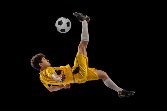 Dynamic portrait of professional football, soccer player training with ball isolated on dark background. Concept of sport, match, active lifestyle, goal and hobby