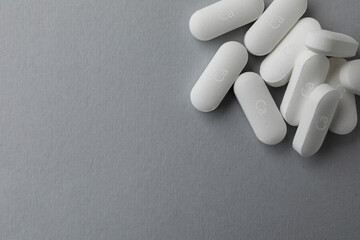 Pile of calcium supplement pills on grey background, flat lay. Space for text