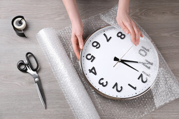 Woman covering wall clock with bubble wrap at wooden table, closeup