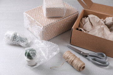 Fragile ceramic decor elements in bubble wrap near cardboard boxes, scissors and twine roll on...