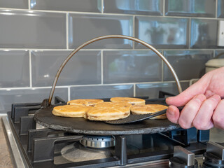 chef turning Welsh Cake over whilst cooking on a cast iron griddle over a gas hob flame