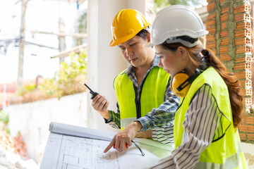 Asian engineer or Young Female Architect put on a helmet for safety and talk with a contractor on a construction building factory project, Concept of Teamwork, Leadership concept.