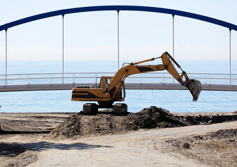 excavation and earthmoving machinery, bulldozer with bridge and sea in the background. Cleaning of the river mouth into the sea. © Fernando