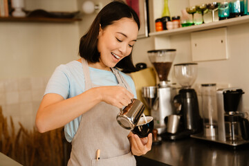 Young asian barista woman smiling while making coffee in cafe